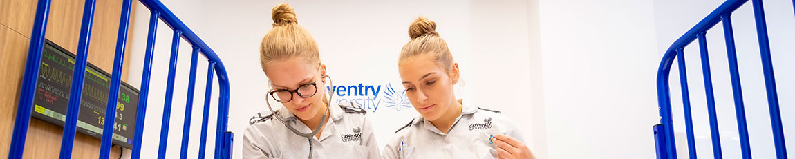 two female student nurses lookin over a hospital bed